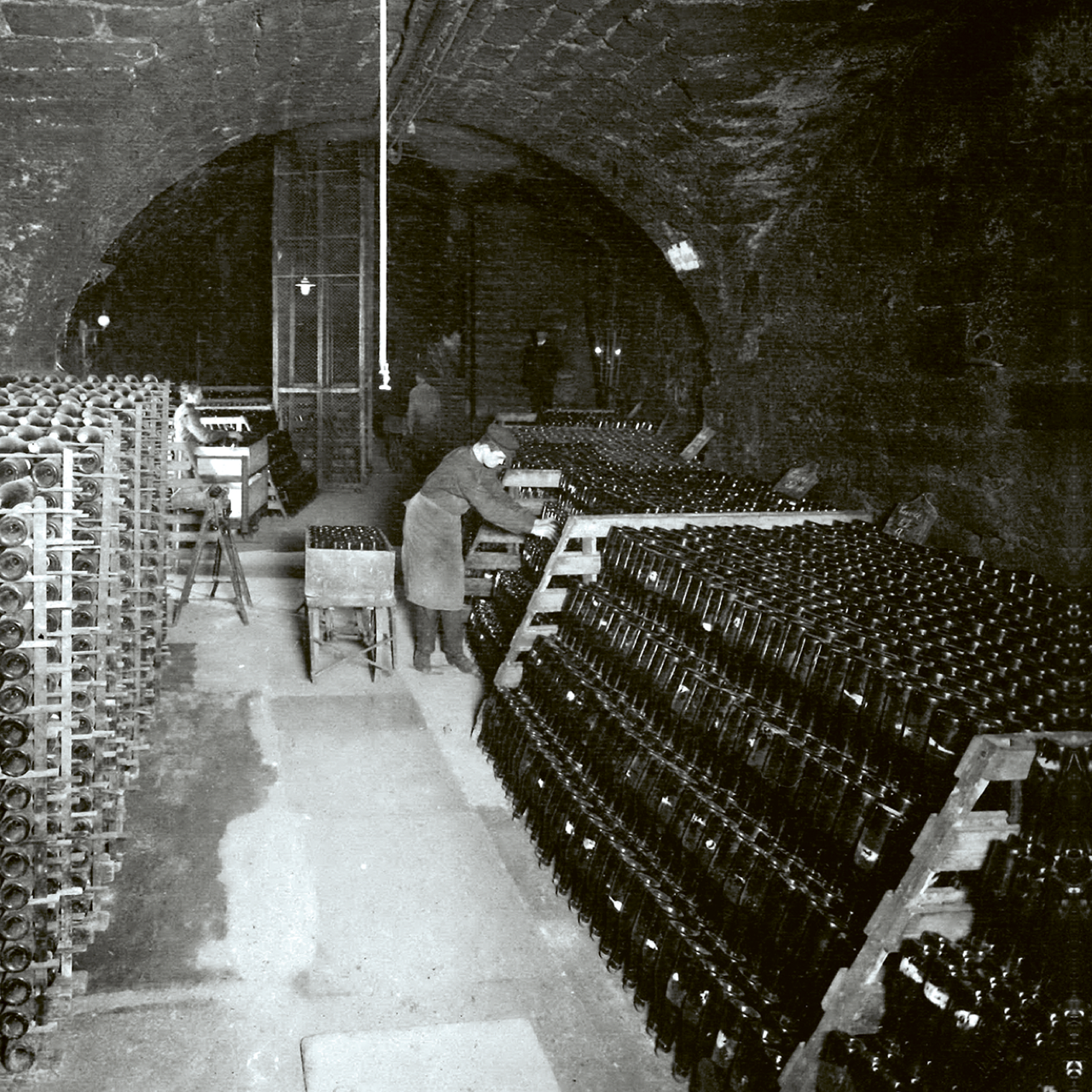 Historischer Gewölbekeller mit gelagerten Sektflaschen und arbeitender Person
