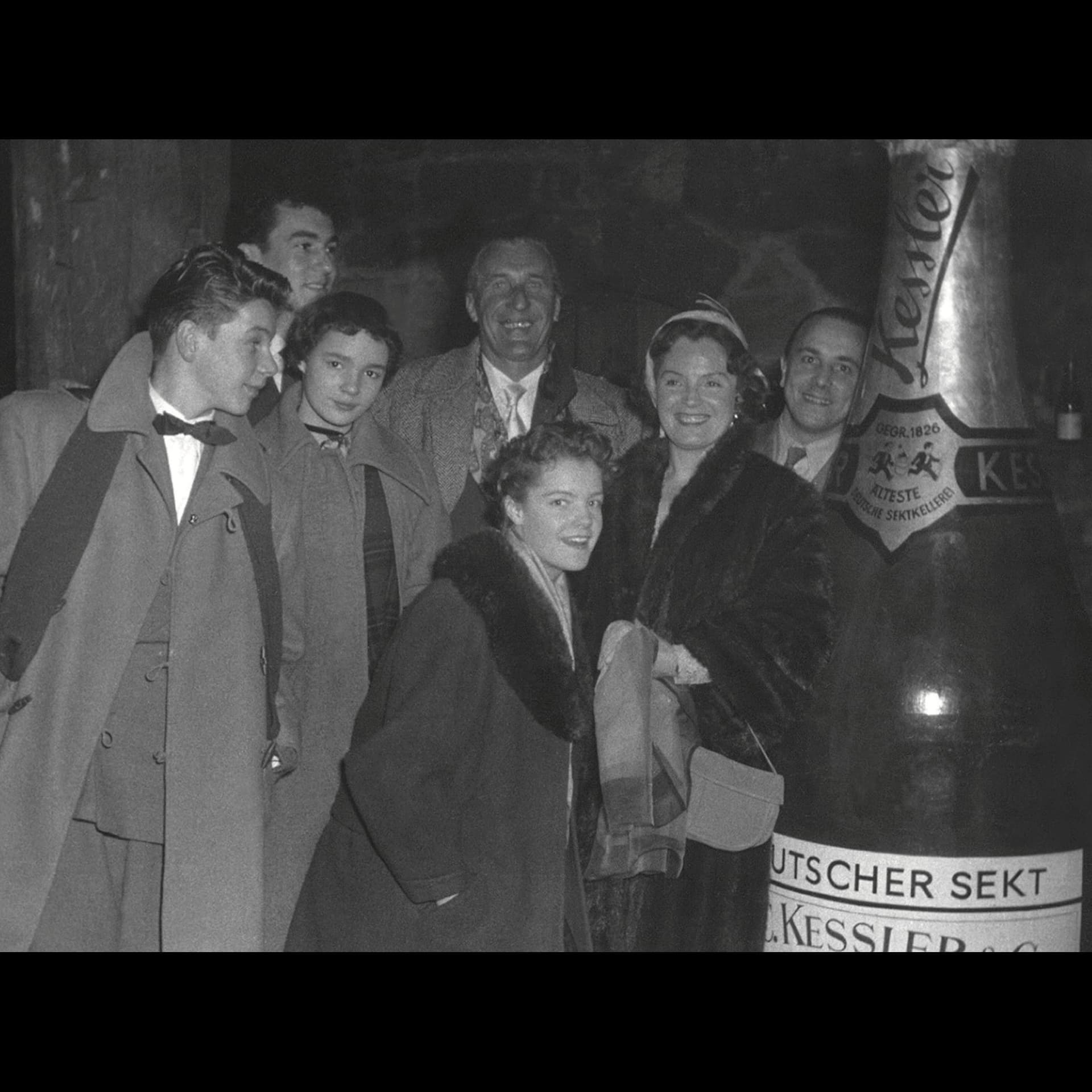 Historische Aufnahme einer Gruppe von Personen neben einer großen Kessler Sektflasche